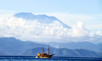 A liveaboard Penesi sailing ship cruises the waters off Nusa Lembongan in the shadow of the mighty Mt Agung